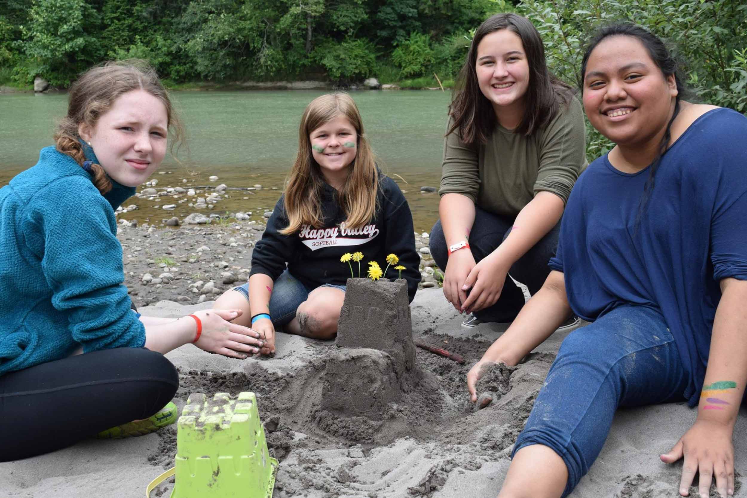 YMCA Camps Group of girls sit in sand by river shore