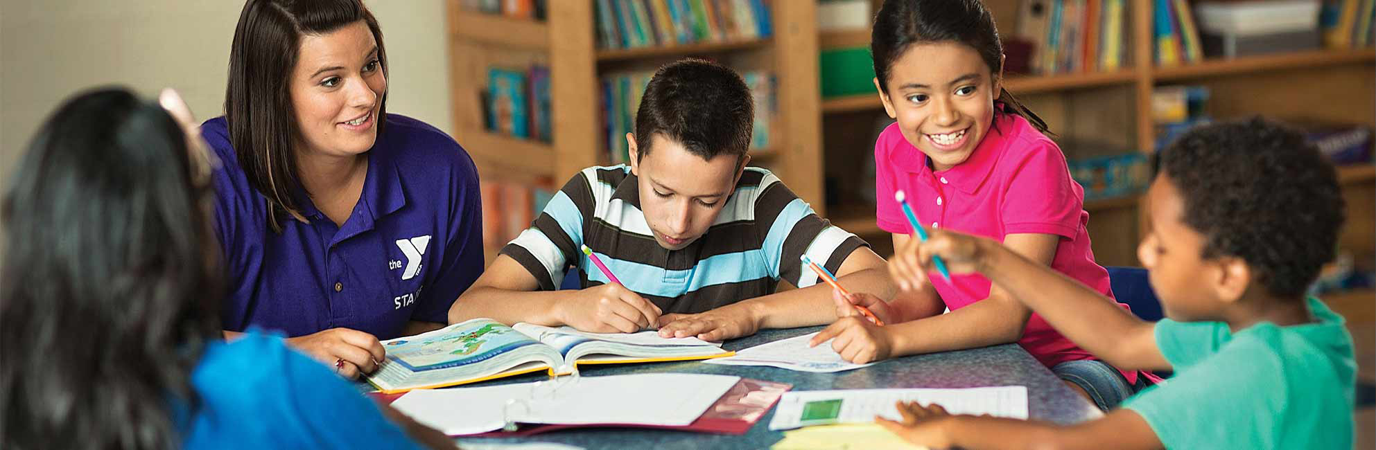 YMCA Volunteer Helps with Homework Tudor helps children with homework at table